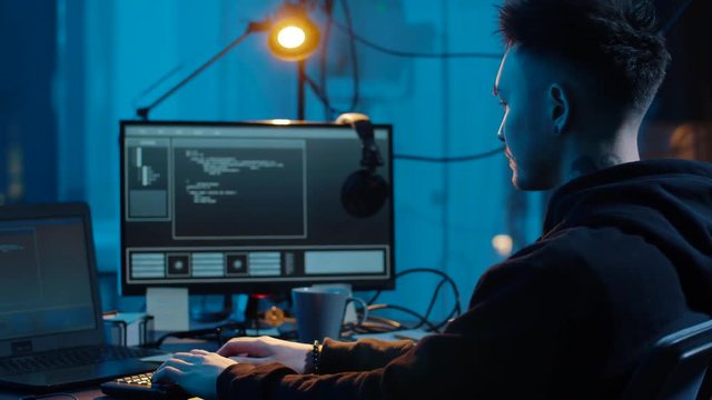 cybercrime, hacking and technology concept - asian male hacker writing code or using computer virus program for cyber attack and drinking coffee in dark room at night