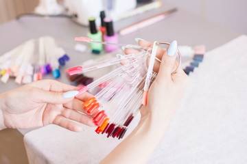 Young woman hands choosing nail color. Female manicured hands and nail color samples.