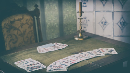 A group of playing cards on an old oak wooden table, a candle stands nearby. Opposite the empty...