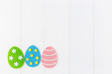 Closeup top view photo of cute diy colorful vivid green, blue, pink 3 eggs decorated with dots, stripes and flowers isolated on white painted wooden background. Happy Easter holiday greeting card.