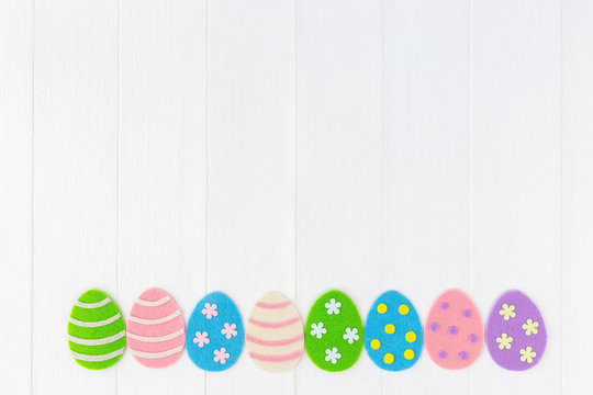 Closeup top view photo of cute diy colorful pastel eggs decorated with dots, stripes and flowers isolated on white painted wooden background. Happy Easter holiday greeting card with blank empty space.