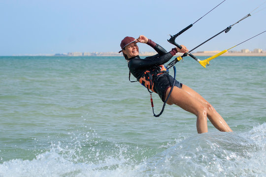 Kite surfing girl in sexy swimsuit with kite in sky on board in blue sea riding waves with water splash. Recreational activity, water sports, action, hobby and fun in summer time. Kiteboarding sport