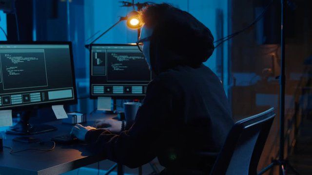 cybercrime, hacking and technology concept - asian male hacker in glasses writing code or using computer virus program for cyber attack and drinking coffee in dark room at night