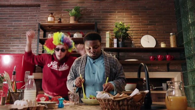 In the kitchen young african american man cook cut salad dance sing at home background man clown dancing smile happy food fresh healthy vegetables dinner portrait close up slow motion