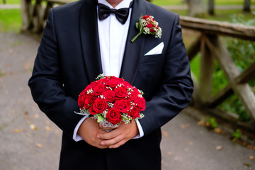 Groom standing in park and holding wedding bouquet of roses. Celebration, holidays and gifts concepts. Wedding day