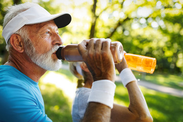 Hydrating. Sporty senior person drinking water in a park