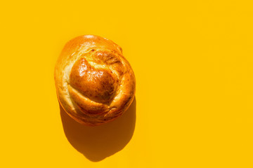 Fresh home baked artisan Easter sweet bread bun on bright yellow background. Trendy style with harsh light hard shadows. Coffee pastry. Holiday baking breakfast morning. Recipe cafe menu template