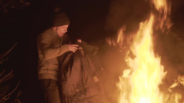 Homeless man plays with his jacket and fire in night forest