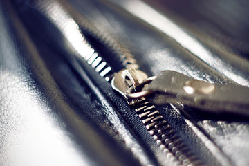 Metal zipper on a black leather bag reflects the sun's bright light