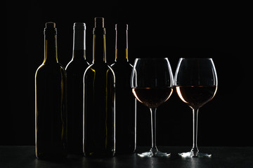 Bottles of wine and different glasses of wine on a dark background