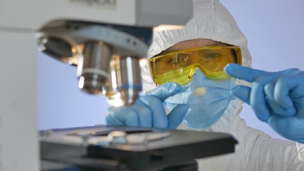 Close-up shot of a scientist looking at a glass slide with bacteria examining with microscope