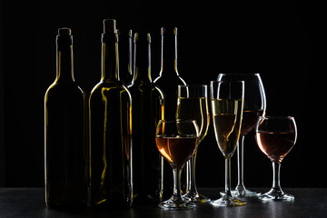 Bottles of wine and different glasses of wine on a dark background