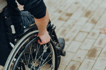 Close-up of male hand on wheel of wheelchair during walk in park