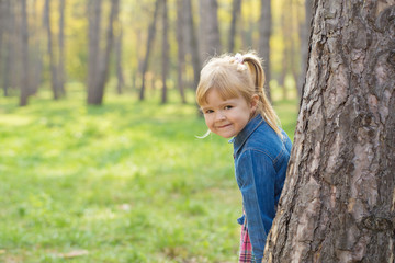 portrait of a happy little girl with a smile on her face hiding behind a tree