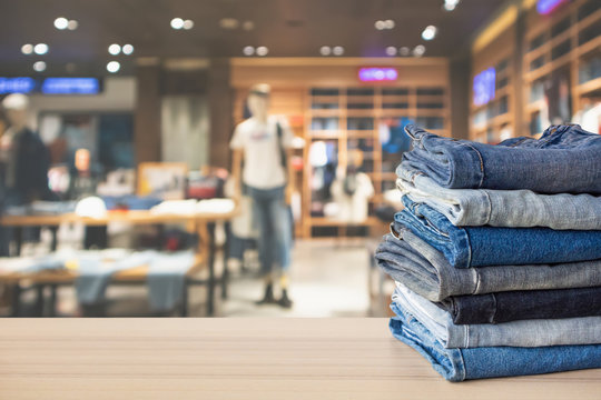 Blue denim jeans stack on wood table top with abstract blur clothing store in modern shopping mall defocused bokeh light background