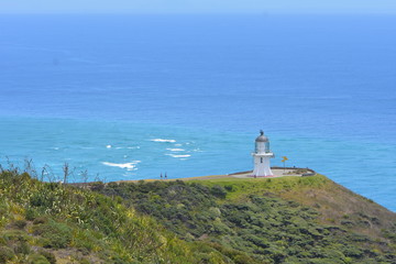 Fototapeta na wymiar Iconic lighthouse at Cape Reinga where Tasman Sea meets Pacific Ocean. Note different colors of sea water.