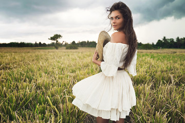 Young lovely woman holding straw hat in the rice field