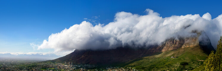 Table Mountain under huge white cloud on blue sky background beautiful landscape panorama, scenery panoramic view of capital city at foot of mountain on sunny day in Cape Town South Africa, copy space