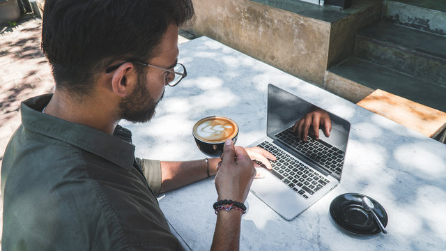 Young man with beard drinking coffee while working on computer at a open air restaurant – Business lifestyle concept – Hustle and grinding – Image