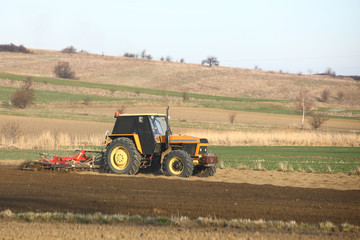 Obraz premium A farmer on a red tractor with a seeder sows grain in plowed land in a private field in the village area. Mechanization of spring field work. Farmer's everyday life. relief of human labor