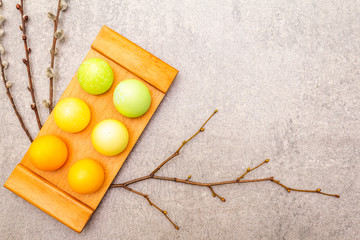 Easter eggs with willow seals branches. Concept on a wooden stand on a stone background, top view, copy space.