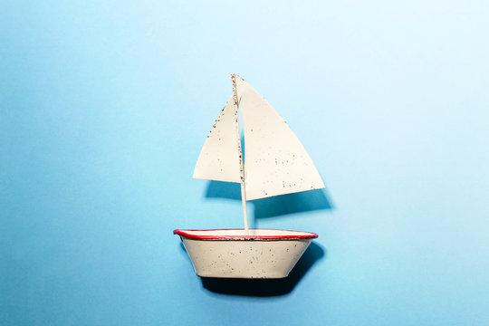 青バックの上に白ブリキのヨットを置いて海を航海しているイメージ