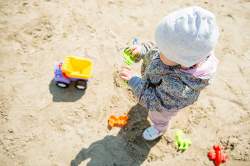 Toddler girl playing in sand on the beach in spring or autumn, leisure activity