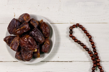 Dates fruit and rosary on white wooden table. Top view