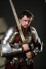 Fototapeta na wymiar Medieval man knight in armor and weapon on dark background. Portrait of the knight