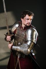 Medieval man knight in armor and weapon on dark background. Portrait of the knight