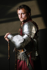 Medieval man knight in armor and weapon on dark background. Portrait of the knight