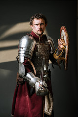 Fototapeta na wymiar Medieval knight in armor holding sword and shield on the dark background