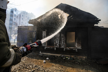 Fireman spraying water in a smouldering burnt out house