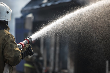 Fireman spraying water in a smouldering burnt out house