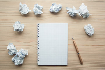 Pad and pencil on wooden bright paper with crumpled paper balls around them. Mockup. Creativity concept. Creation, writing symbol.