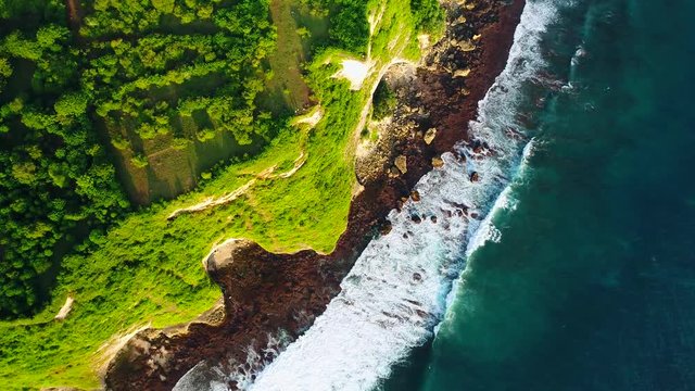 Aerial, screwdriver, drone shot above the Karang boma cliff, while waves crashes on the rocky coast, on a sunny evening, in Uluwatu, in Bali, Indonesia - 4k Footage