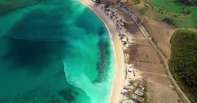 Aerial, top down, drone shot above turquoise sea and a white sand shore, clouds shades moving on the ground, on a sunny day, at Mawun beach, in Lombok, Indonesia