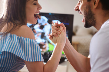 Couple watching soccer game on television, celebrating goal screaming taking five and hugging