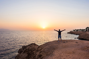 Traveller man with backpack on the beach over sunrise background