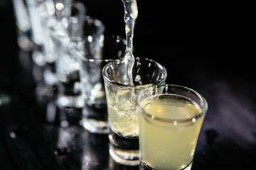 Bartender making yellow alcohol shots, black counter, black background.