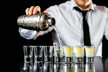 Bartender making yellow alcohol shots, black counter, black background.