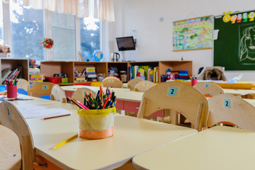 Room in elementary school, interior with light wooden furniture and learning aids on the walls. Pencils on the tables. No one, the children went for a walk