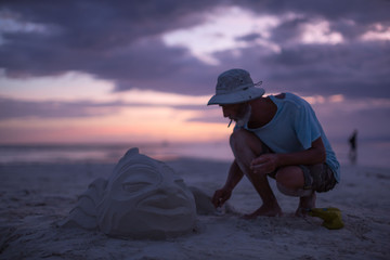 man modeling an artistic fish sculpture out of sand at a white beach a summer vacation scene - Powered by Adobe