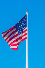 The flag of the United States of America sways in the wind on flagpole against a background of clear blue sky.