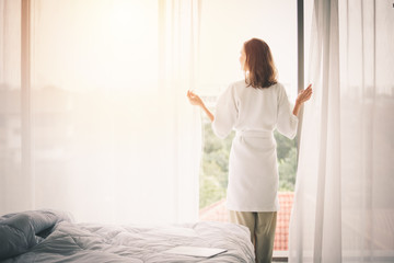 view back woman opening curtains in a white bedroom