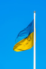 The flag of Ukraine are sways in the wind on flagpole against a background of clear blue sky