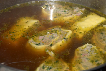 swabian ravioli  filled with spinach and meat in the soup as an appetizer, homemade rolled swabian meat ravioli floating in hot broth in a metal pot