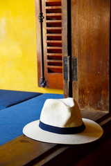 Beach hat on the window edge with yellow wall, wooden window frame and blue pillows in the background