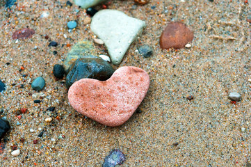 A heart-shaped sea rock on a sandy background. A heart of red stone.	