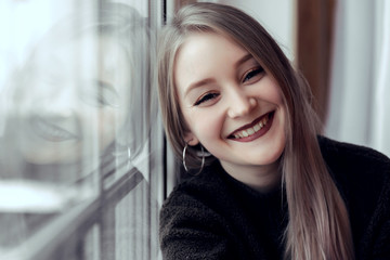 beautiful young girl sitting alone on the windowsill and looking at the camera and smiling.